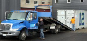 Blue delivery truck in front of gray shipping container