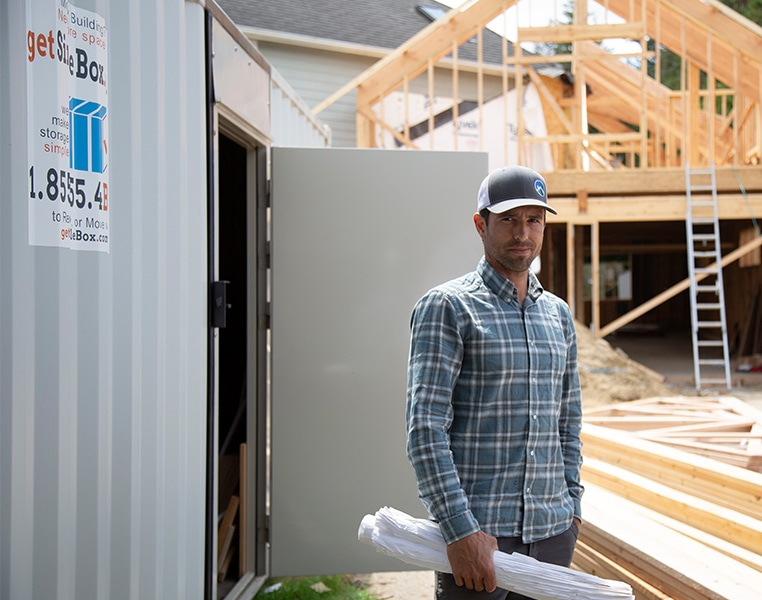 Man standing next to a rented storage container in front of a house that is under construction