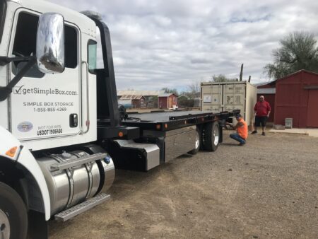 Image shows delivery of a 20-foot Shipping Container. The Delivery truck is white with a black deck and the container is tan.