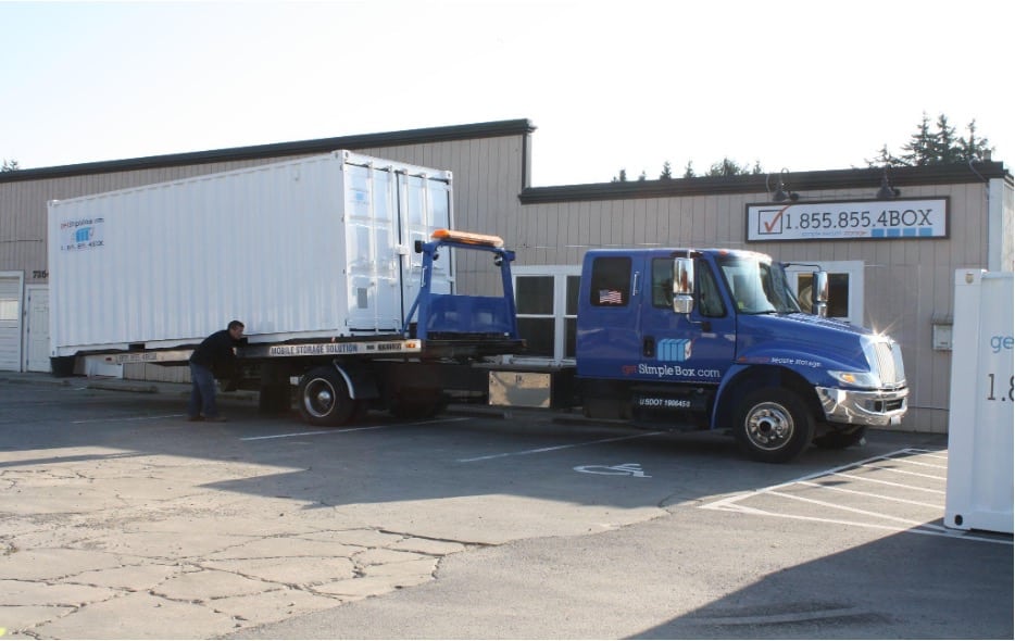 Shipping container being delivered with tilt bed trailer