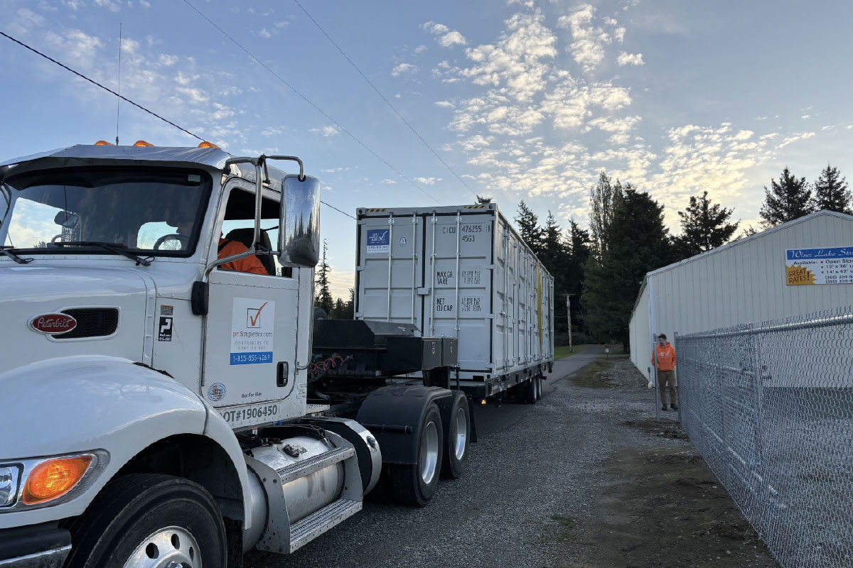 This photo includes a driver in a truck delivering a shipping container to an individual who wanted to know how fast they can rent a shipping container.