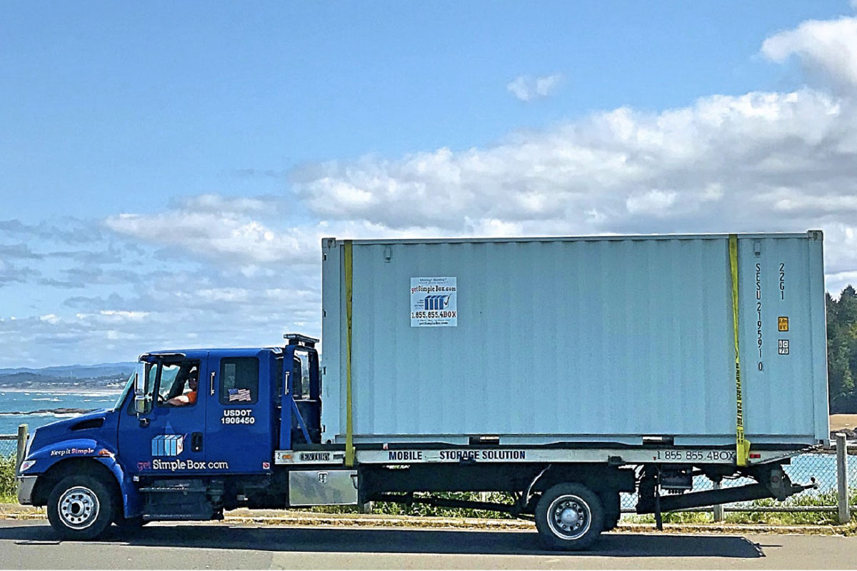 20 foot shipping container on the road on its way to get delivered with a blue sky and a lake at the back
