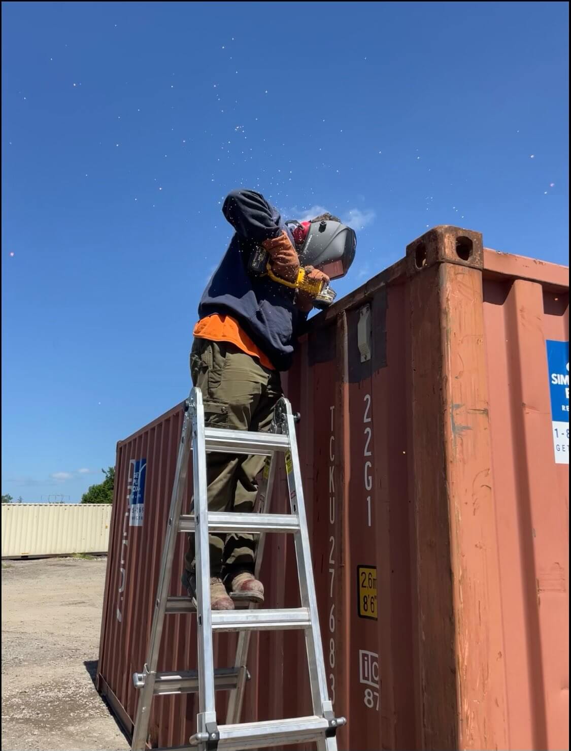 Steppan on a ladder completing container modifications in Salem to a red shipping container