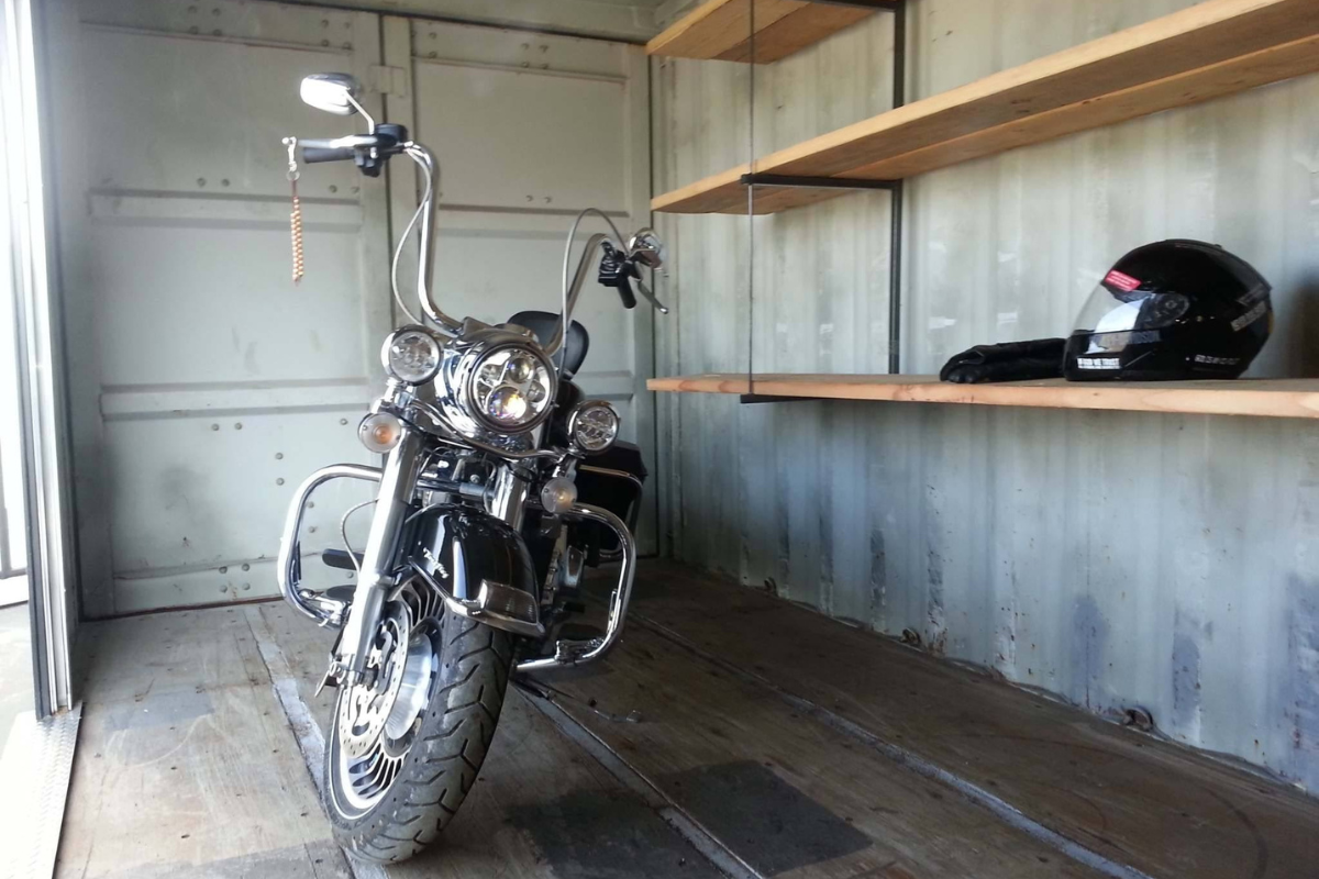 A motorcycle parked inside a storage container with loft-style shelving and organized gear