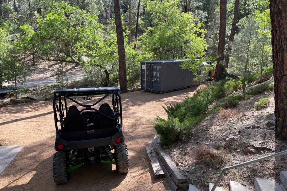 A storage container placed in a rugged outdoor setting with a side-by-side parked beside it