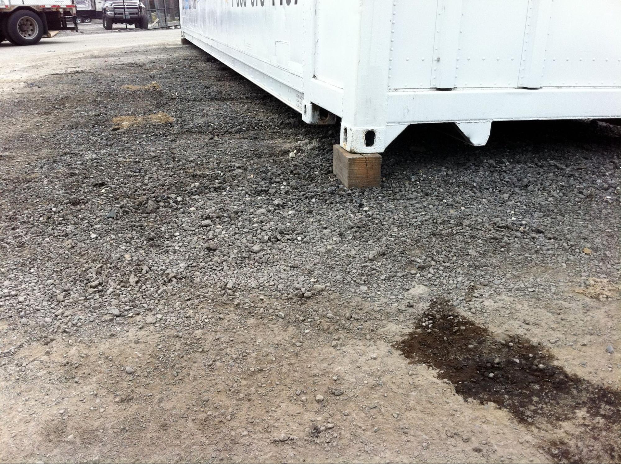 A 20-foot shipping container placed level on a compacted gravel pad with pressure-treated wood blocks under the steel corner castings.