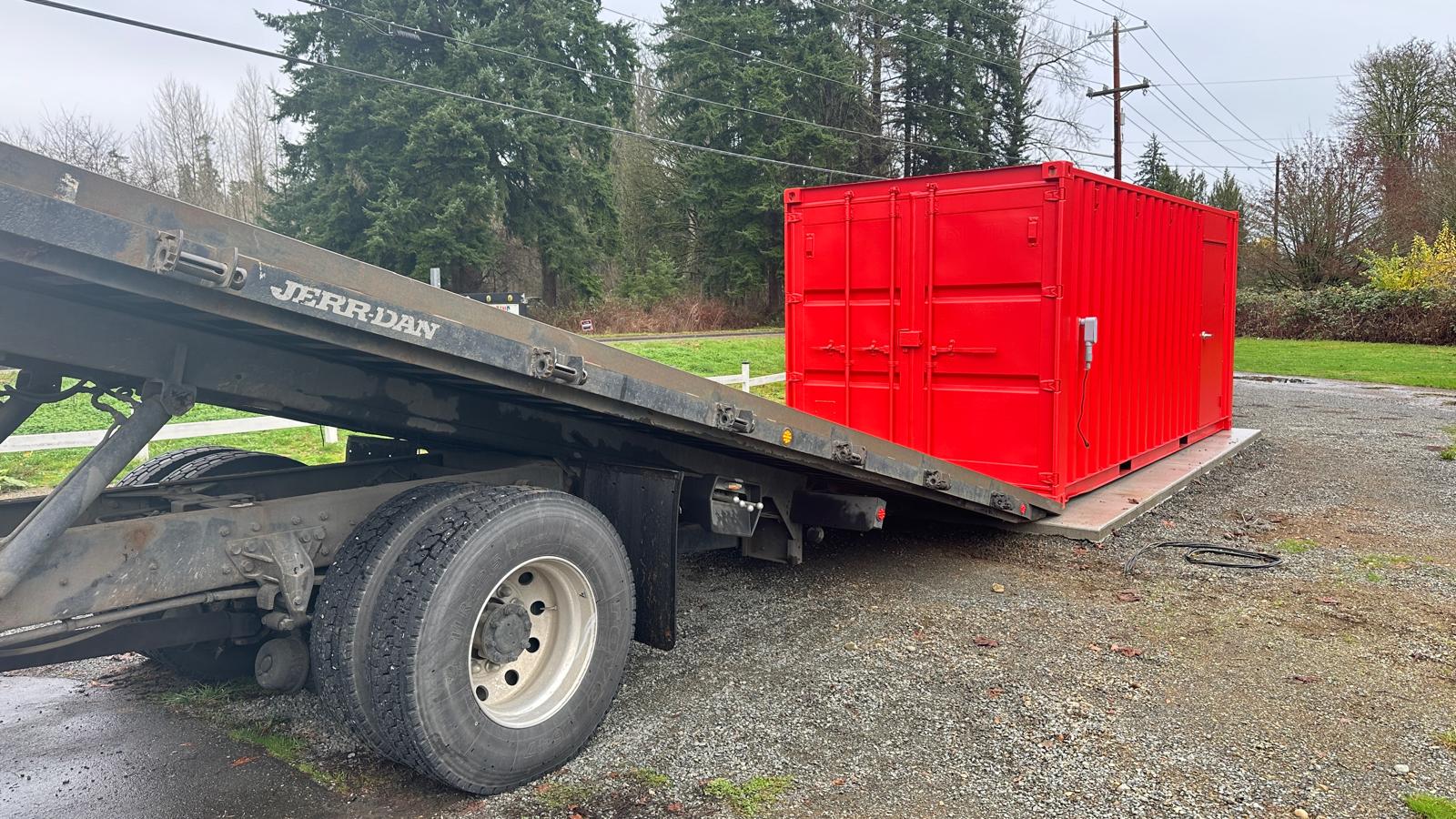 A Get Simple Box tilt-bed truck delivering a shipping container rental in Dallas, OR, precise placement on a leveled gravel pad ensures proper airflow underneath the unit