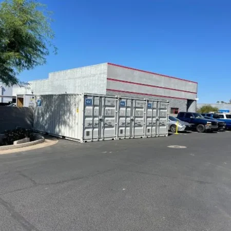 Row of white shipping containers placed outside a commercial building parking lot