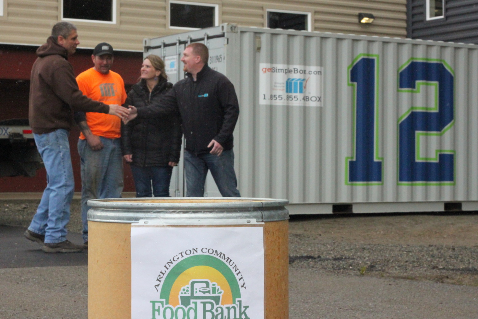 Team members donating to a local food bank in front of a container with a number 12