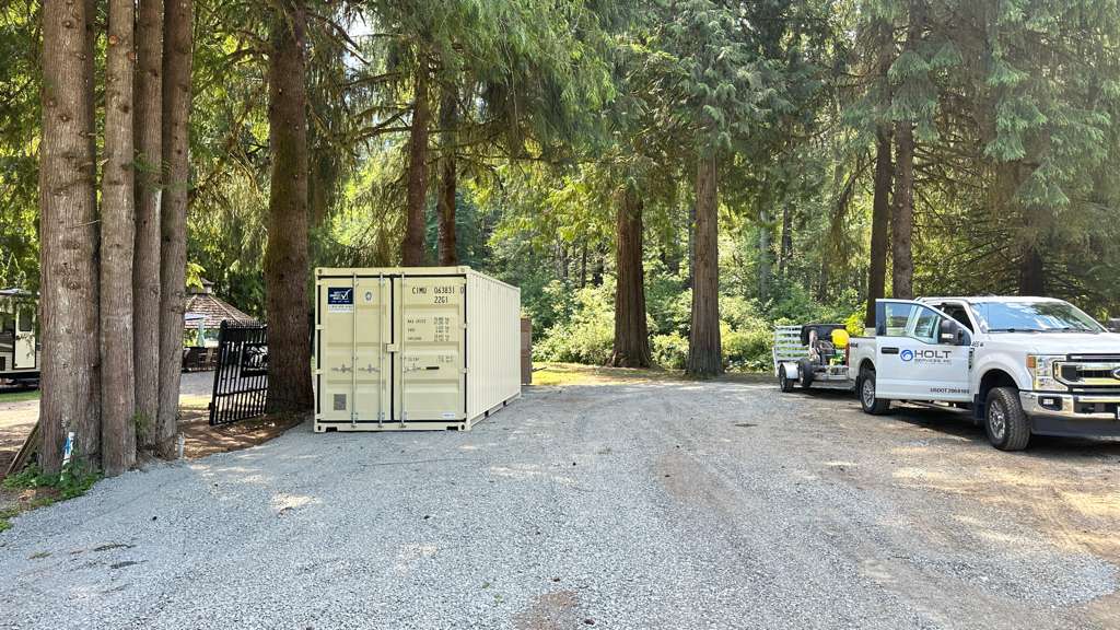 Tan storage container on a gravel lot surrounded by tall trees