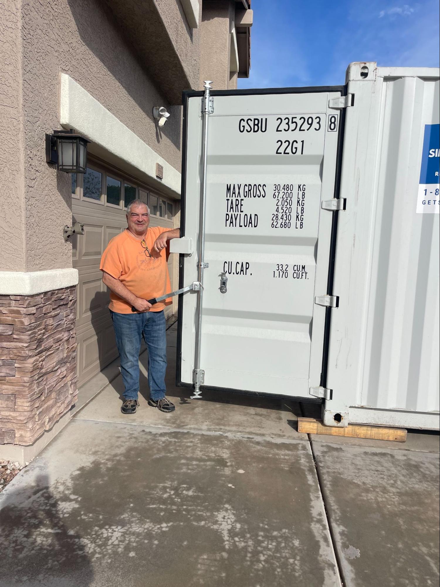 delivery operator checking the clearance of a container door mechanism near a home garage wall, ensuring total accessibility for the customer.
