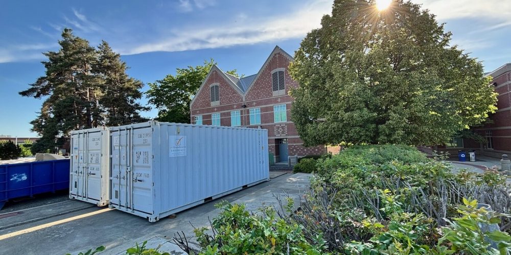 Two white storage containers outside a brick building