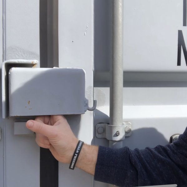 a hand opening a small metal door lockbox on a storage container