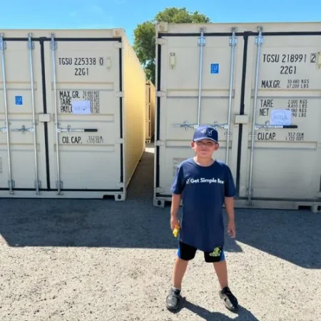 Boy standing in front of two white shipping containers in a storage yard