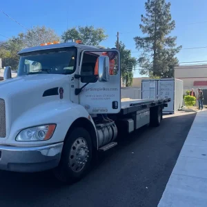 Delivery truck unloading a storage container beside a building with crew nearby