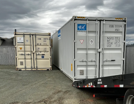 Tan and white containers, one on a trailer, under a cloudy sky